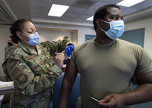 An image of a uniformed member giving a vaccination shot to another
